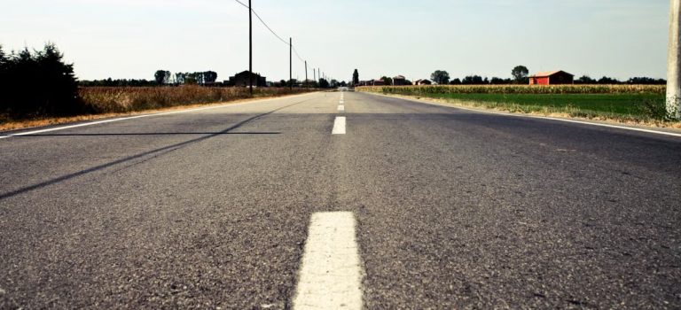A tranquil countryside road in Calderara di Reno, Italy, with clear blue skies and open fields.